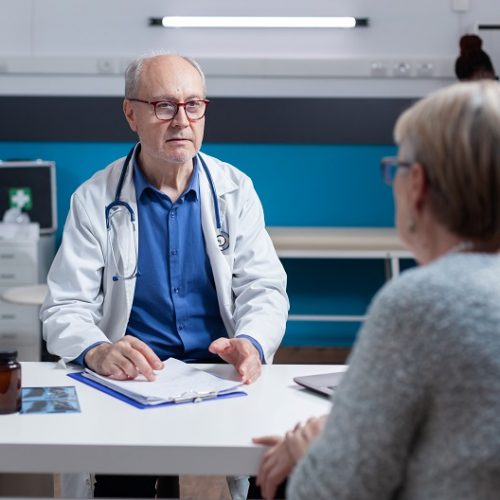 Physician attending consultation appointment with aged patient in office. Healthcare specialist and woman having conversation about disease diagnosis at annual checkup visit. Medical exam