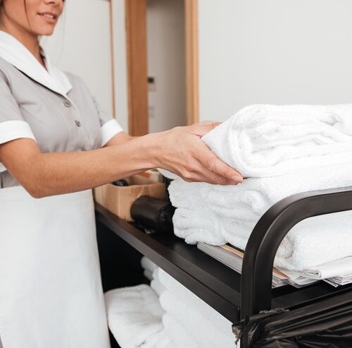 Cropped image of a smiling young maid taking fresh towels from a housekeeping cart